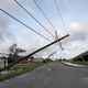 A electrical pole and line is seen leaning steeply over a road, damaged by a hurricane.